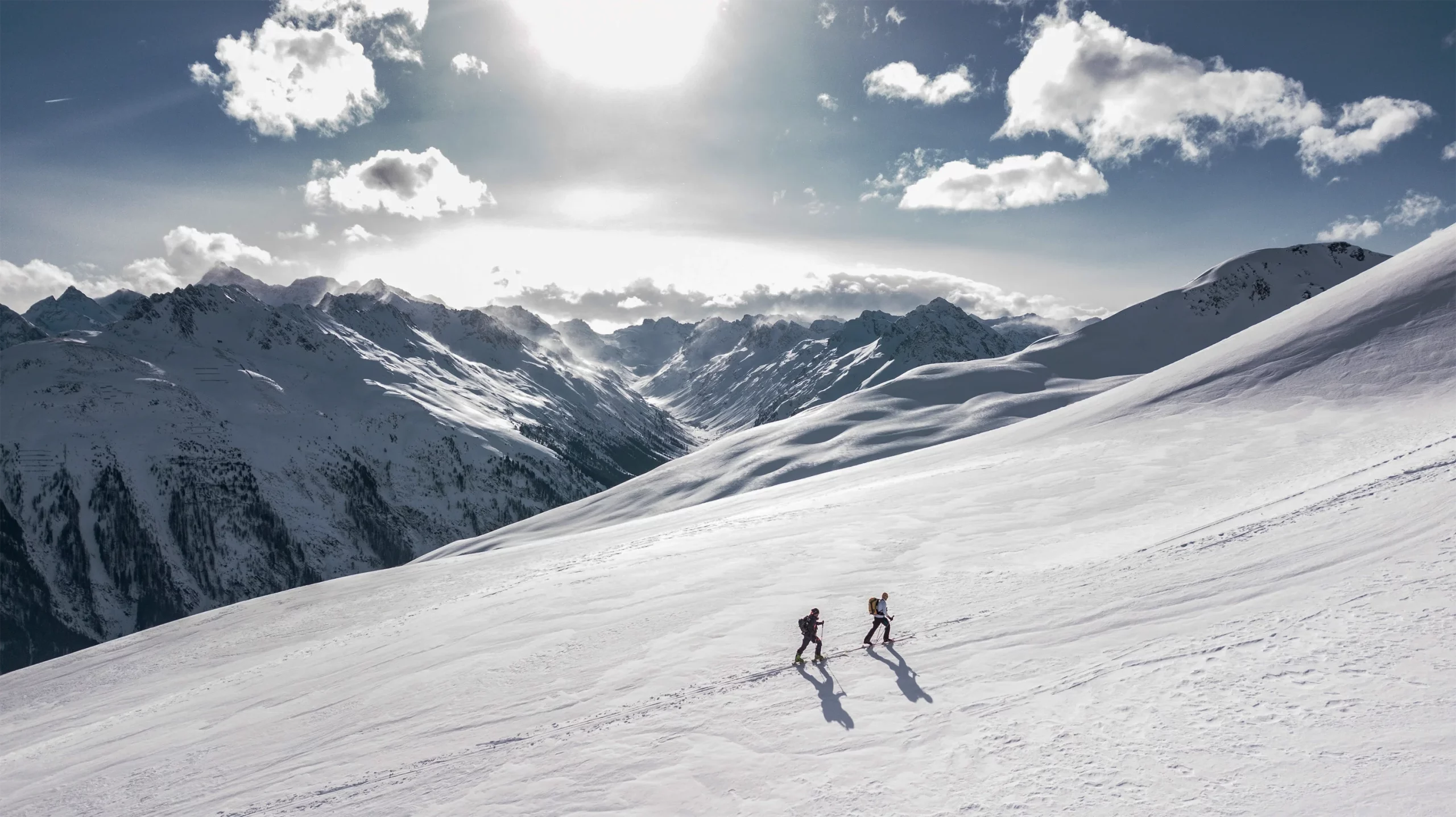 Deux personnes marchent ensemble dans une plaine enneigée au milieu des Alpes suisses.